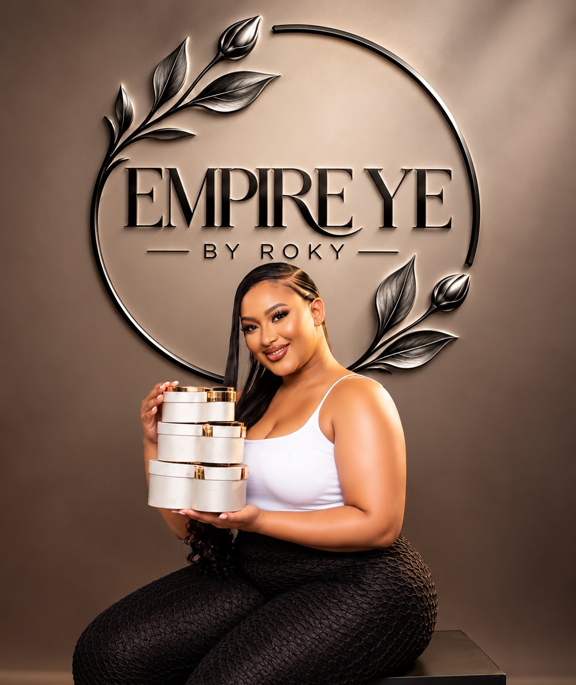 Roky assise devant le logo Empire Ye, tenant les boîtes rondes à couvercle doré